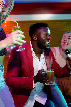 Vertical of happy african american man and diverse female friends singing karaoke at nightclub bar