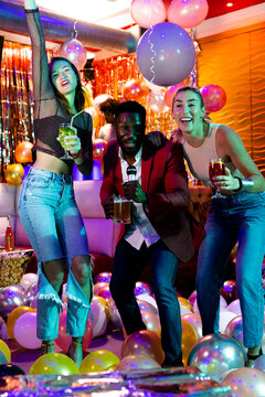 Vertical of three happy, diverse male and female friends singing karaoke, drinking at nightclub bar