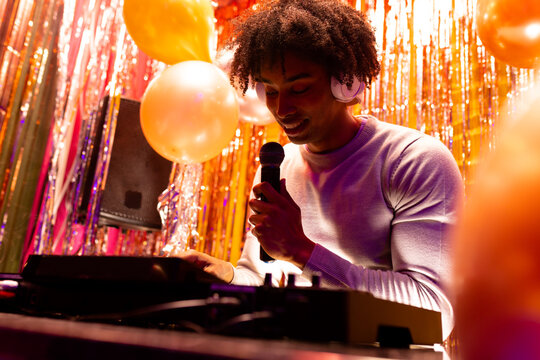 Smiling african american dj in headphones playing music at a nightclub and using microphone