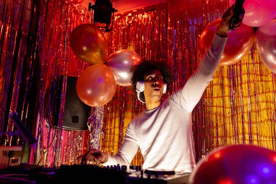 African american dj in headphones playing music at a nightclub and holding microphone