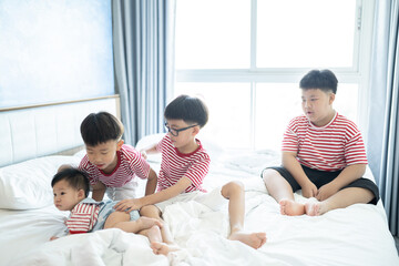Fototapeta premium Brothers and baby sister is playing on the white bed in the bedroom.The selective focus and space for copy and text.