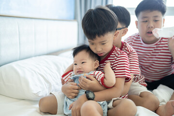 Brothers and baby sister is playing on the white bed in the bedroom.The selective focus and space for copy and text.