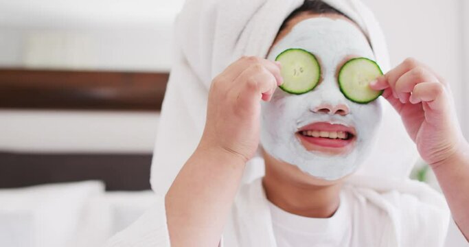 Video of happy asian girl in robe doing cucumber mask and having fun