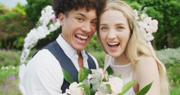 Portrait of happy diverse couple holding hands with ring on sunny day at wedding