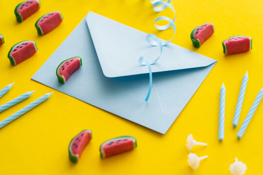 Envelope near festive candles and sweets on yellow background.