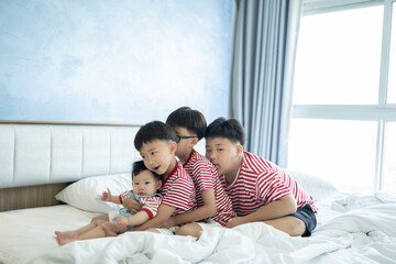 Brothers and baby sister is playing on the white bed in the bedroom.The selective focus and space for copy and text.