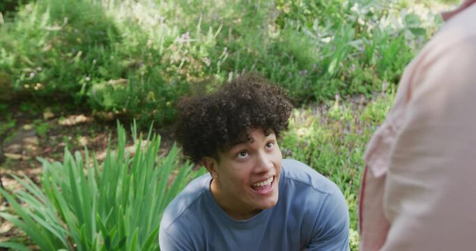 Happy diverse couple proposing and smiling in garden on sunny day