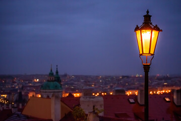 A shining lamp above the Prague cityscape in the evening.