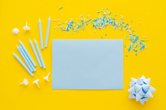 Top view of empty greeting card near candles and blue sprinkles on yellow background.