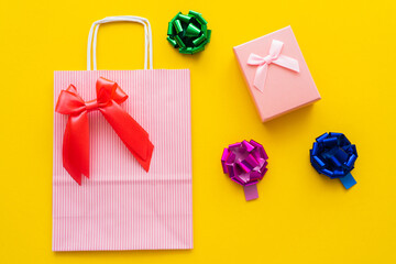 Top view of shopping bag and gift bows near present on yellow background.