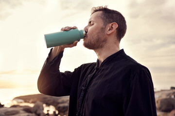 Drinking water, fitness and nature with a sports man or running taking a break on the beach during...