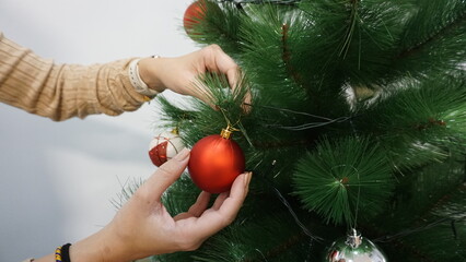 Decoración Navideña. Manos decorando el árbol de Navidad con bolas blancas y rojas. 
