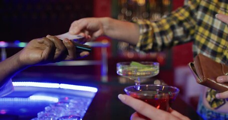 Video of midsection of diverse barman and female customer paying for drinks by credit card at bar