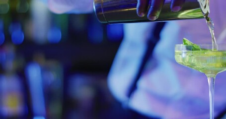 Video of midsection of african american barman preparing green cocktail at the bar