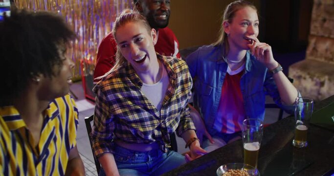 Video of diverse group of happy friends drinking and reacting to sports game on tv at a bar