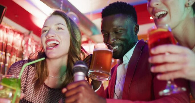 Video of diverse happy group of friends signing karaoke and drinking at a nightclub bar