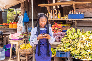 young black African businesswoman in a local market browsing online using smartphone checking...