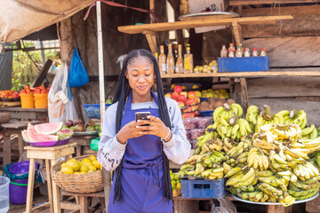 young black African businesswoman in a local market browsing online using smartphone checking reading news online