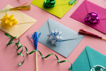 Close up view of colorful envelopes with gift bows near serpentine on pink background.