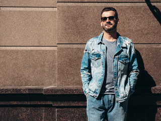 Obraz premium Portrait of handsome confident stylish hipster model. Sexy man dressed in jeans jacket. Fashion male posing in the street. In Europe city. Outdoors at sunny day. In sunglasses