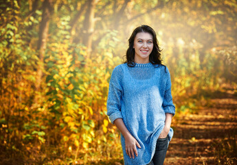 Smiling young brunette posing in park on background of trees with orange leaves