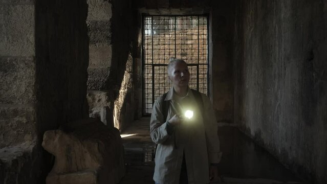 A young female archaeologist walks down a dark corridor to the cell with a flashlight in her hands. High quality 4k footage