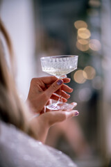 The hands of a woman hold a glass of champagne on a background of golden beke. The concept of the holiday, Christmas, new year, birthday.