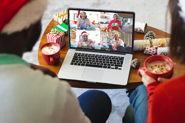 Diverse couple with christmas decorations having video call with happy diverse friends