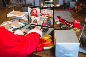 Santa claus with christmas presents having video call with happy caucasian children