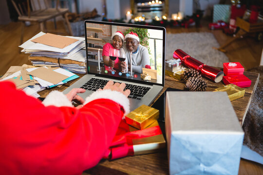 Santa claus with christmas presents having video call with happy african american couple