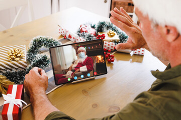 Caucasian man with santa hat having video call with santa claus with face mask