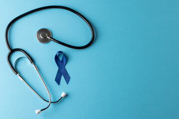 Composition of blue cancer awareness ribbon and stethoscope on blue background with copy space