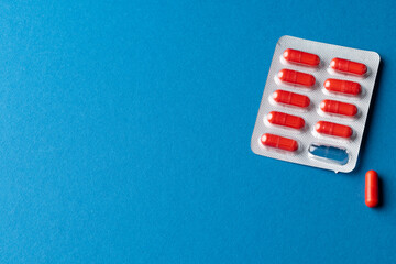 Composition of red pills in blister pack, and one pill out, on blue background with copy space