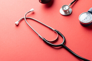 Composition of sphygmomanometer and stethoscope on red background with copy space