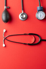 Vertical composition of sphygmomanometer and stethoscope on red background with copy space