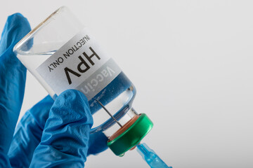 Composition of doctor's gloved hands filling syringe from hpv vaccine vial, on white with copy space