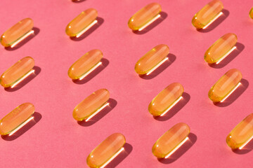 Composition of oil capsules arranged in rows on pink background