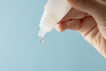 Composition of hand holding dropper bottle with falling drop, on blue background with copy space