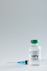 Vertical composition of hpv vaccine vial and syringe on grey background with copy space