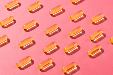 Composition of oil capsules arranged in rows on pink background