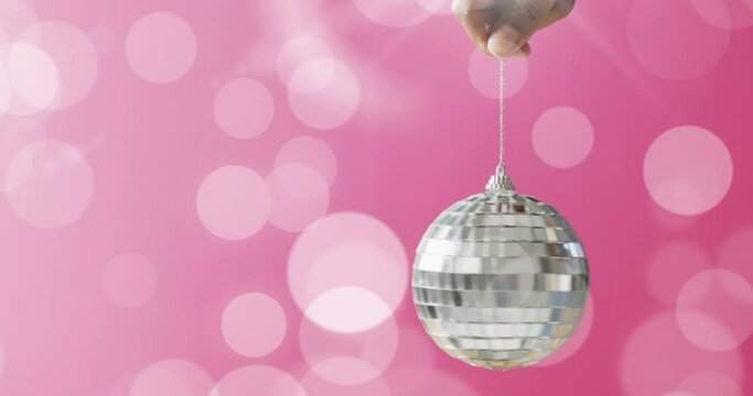 Animation of silver bauble and white spots of light on pink background