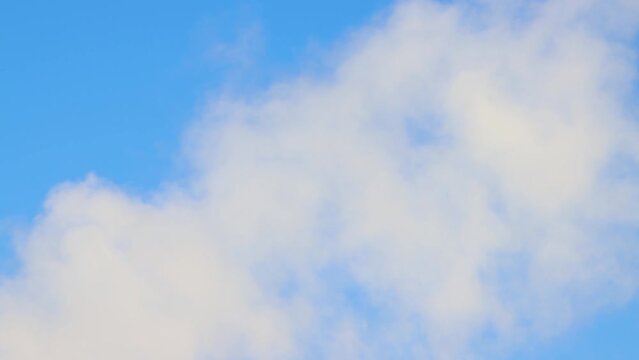 A white fluffy cloud moves from left to right against a blue sky. Summer or winter time lapse, clear sky, warm light, panorama. Video, screensaver background, for titles, intro, transition. UHD 4K.