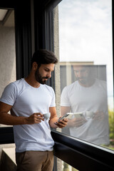person using a phone, handsome boy looking at his phone next to a window in his room worried