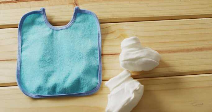 Video of close up of blue baby bib with white booties on wooden background