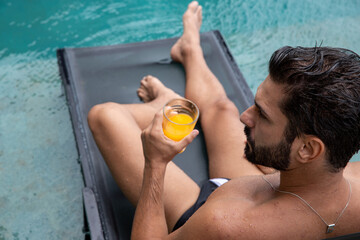 man holding a glass of juice, top view, bearded man, black swimming trunks inside the pool