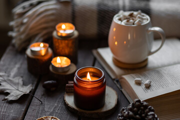 Autumn cozy home composition with hot chocolate with marshmallow and candles. Aromatherapy on a grey fall morning, atmosphere of cosiness and relax. Wooden background, books, close up.