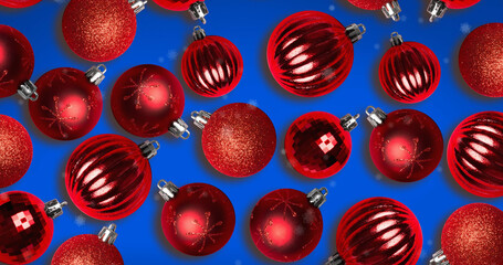 Image of snow falling over christmas bauble decorations on blue background