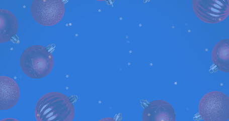 Fototapeta premium Image of snow falling over christmas bauble decorations on blue background