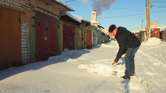 A man clears the passage to the garage from snow with a wooden shovel. Large snowdrifts around after a snowstorm, sunny day. City life, heavy snowfall. UHD 4K.