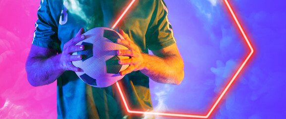 Midsection of biracial male player holding ball with illuminated hexagon shape on colored background